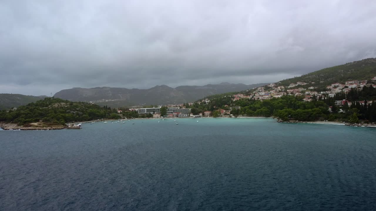 Aerial Drone footage flying into the bay of Mlini over the crystal blue water into the harbour with boats and mountain surrounding