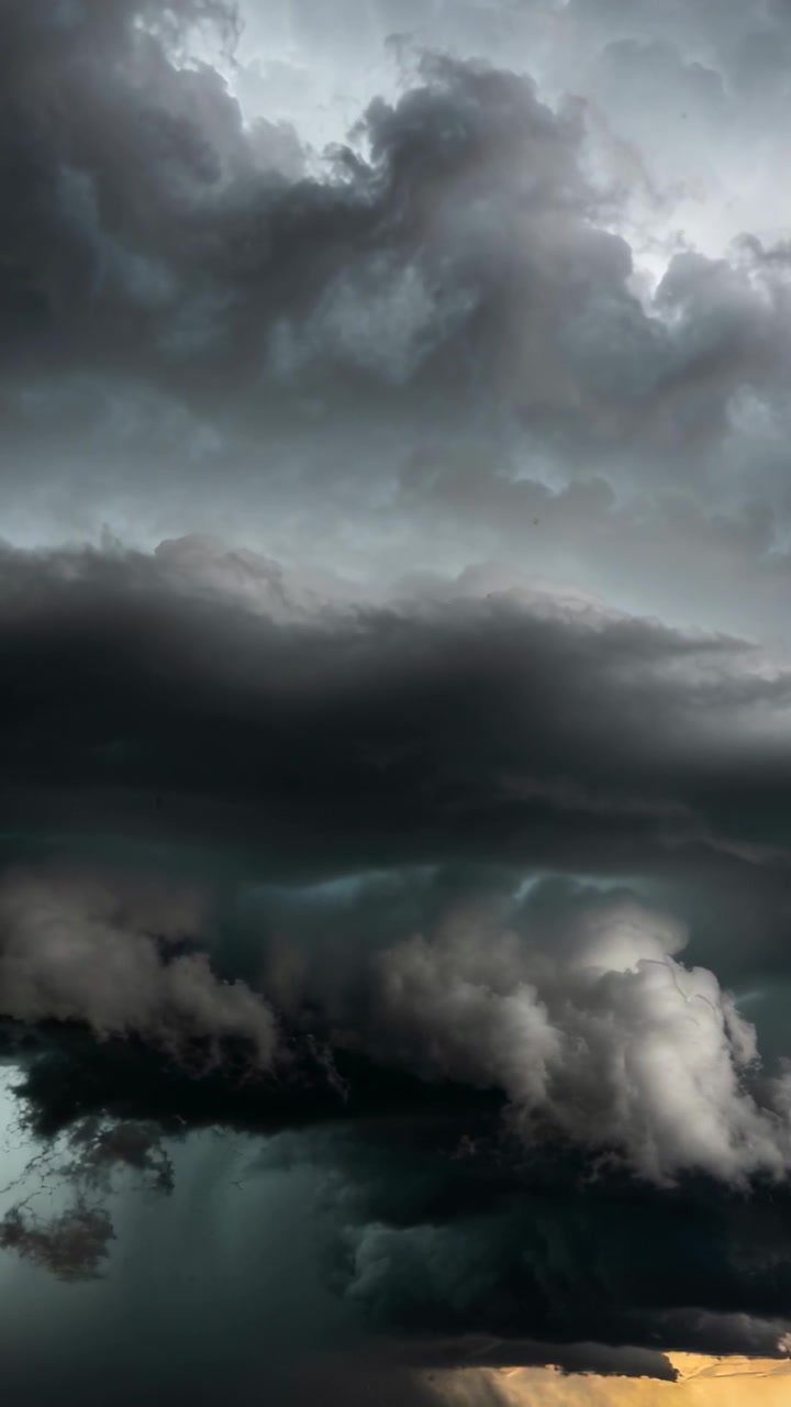 Video vertical: Nube de estante avanzando, bajando su base y formando cortinas de lluvia sobre un horizonte bajo con árboles.