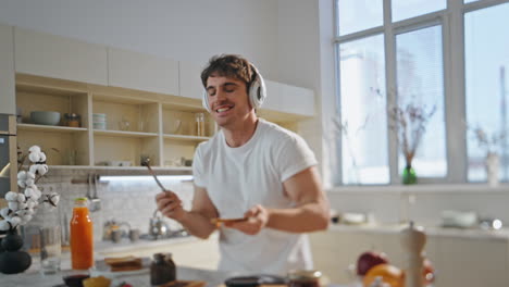 hombre con auriculares preparando comida bailando en casa de cerca. hombre escuchando música en la cocina