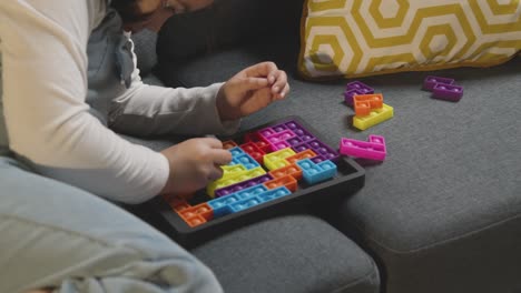 young girl on asd spectrum at home sitting on sofa solving shape puzzle 4