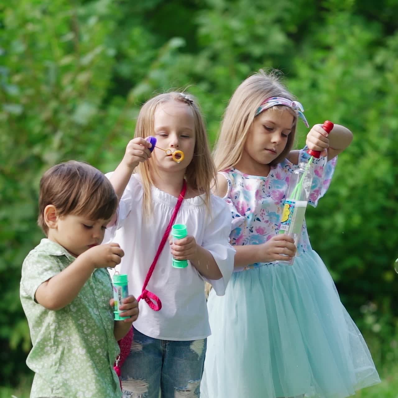 . Happy kids in the park. Little girls blowing soap bubbles in park