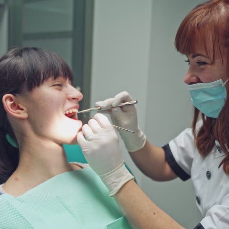 an experienced dentist in a white robe and mask examines the girl's teeth using a dental mirror and tweezers. close-up.
