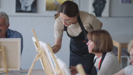 high angle view of cheerful senior friends painting on canvas. senior woman smiling while drawing with the group. seniors attending painting class together. senior men having fun painting in art class