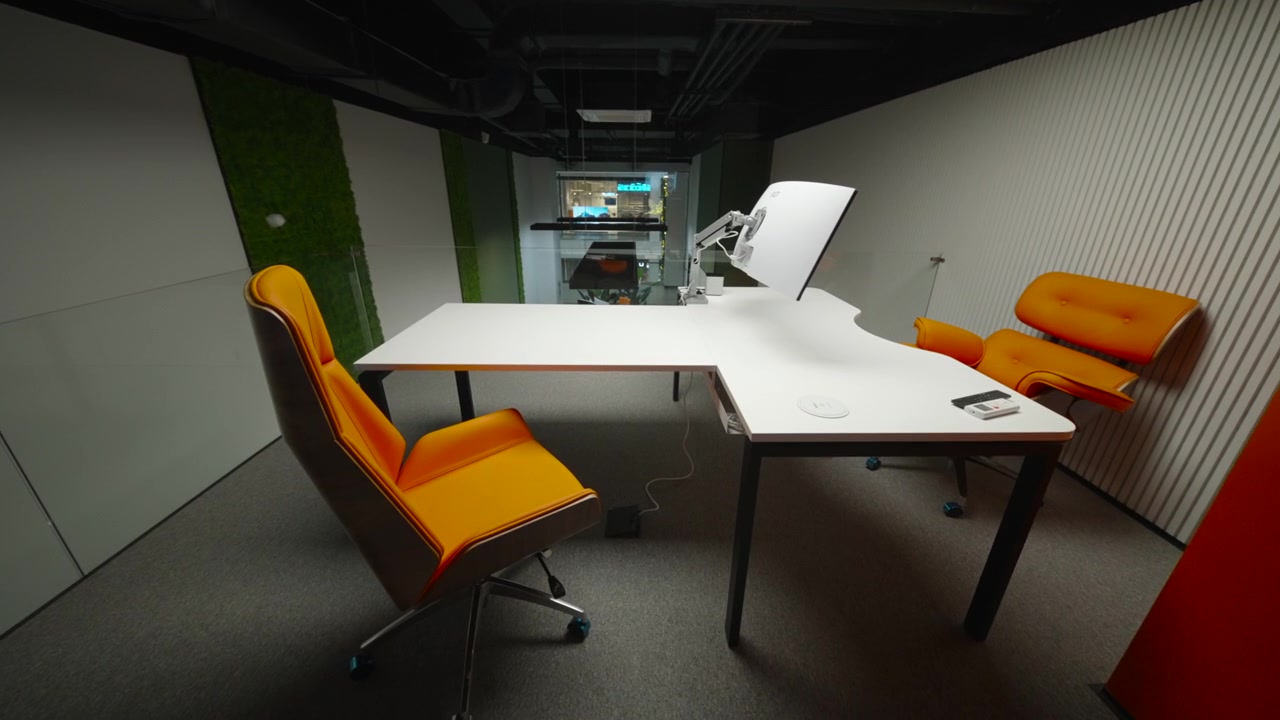 Un elegante interno di ufficio moderno con un tavolo da riunione bianco centrato nella stanza, sedie imbottite arancioni intorno ad esso e un monitor di computer sulla scrivania.