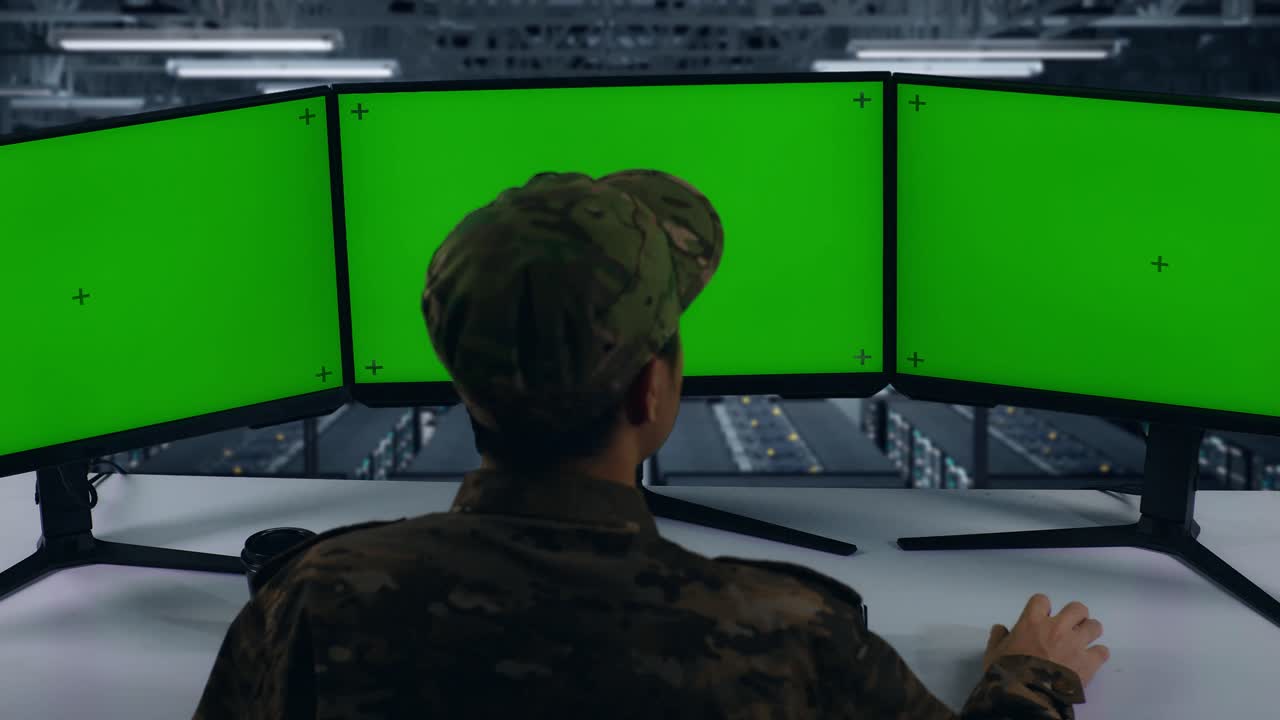 vista de atrás de los militares asiáticos pensando en algo luego levantando su dedo índice mientras trabajaba con simulacro de múltiples monitores de computadora en el centro de datos