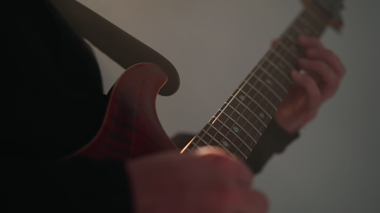 primer plano de una mano tocando una cuerda de guitarra roja contra un telón de fondo borroso