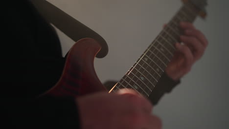 close-up of a hand strumming a red guitar string against a blurred backdrop