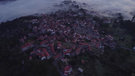 Reveal-shot-of-Monsanto-mountain-village-Portugal-with-low-clouds,-aerial