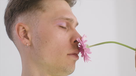 apuesto joven con arete oliendo una flor