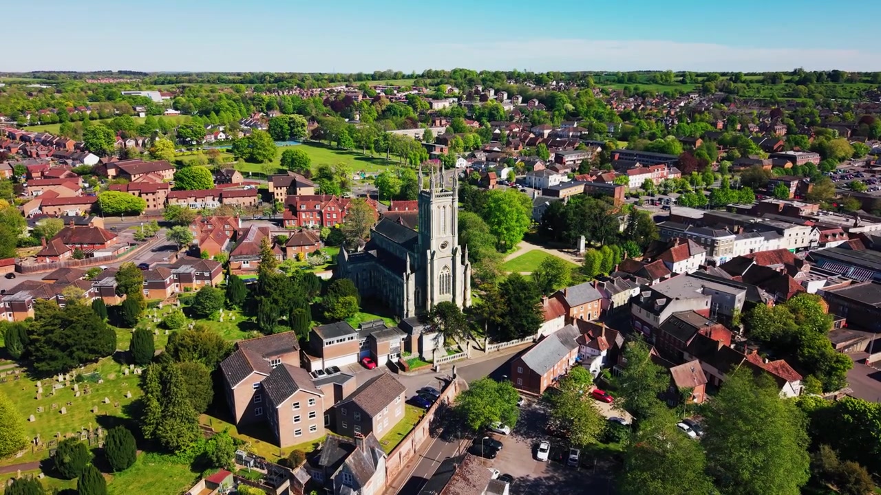 Ampia ripresa aerea con drone della Chiesa di Santa Maria ad Andover, che mostra lo storico campanile, il sagrato, le strade circostanti, i tetti, gli spazi verdi e il più ampio paesaggio urbano in una giornata di sole.