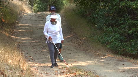 a blind woman walks with a cane through a natural area with a guide helping her explore the wilderness 2