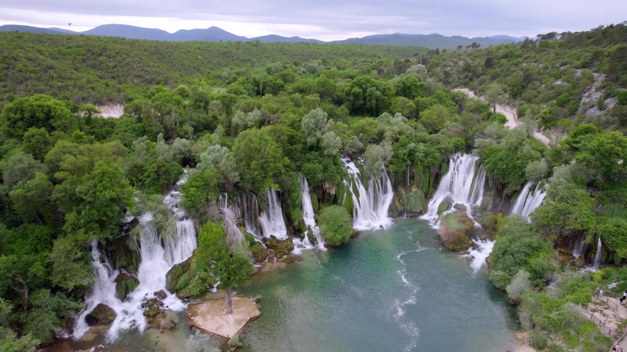 La Cascata di Kravica si estende su un bacino boscoso sotto colline distanti in Erzegovina, ripresa aerea panoramica in dolly