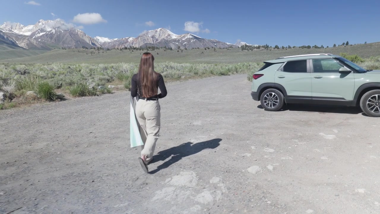 Donna che cammina verso l'auto a Mammoth Lakes, California, con montagne innevate e sorgenti termali, vista posteriore, all'aperto, durante un'avventura di viaggio in una giornata di sole.