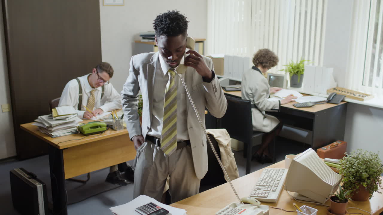 African american businessman working stading near his desk and talking on the phone in a vintage office.