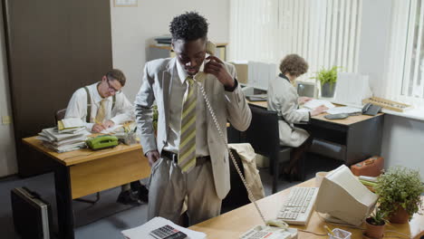 african american businessman working stading near his desk and talking on the phone in a vintage office.