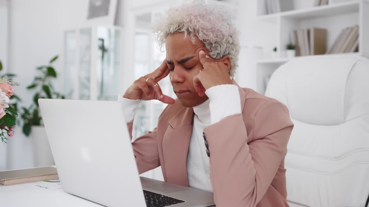 Erschöpfte junge afroamerikanische Frau reibt sich die Schläfen, sitzt am Laptop und hat Kopfschmerzen