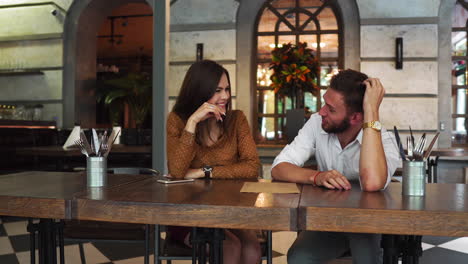 una buena pareja está sentada juntos en un restaurante. ella está bebiendo té y mirando un menú mientras su amigo está tratando de elegir comida para ellos. también le está dando consejos de comida.