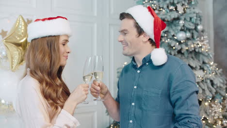 una pareja feliz bebiendo champán cerca del árbol de navidad.