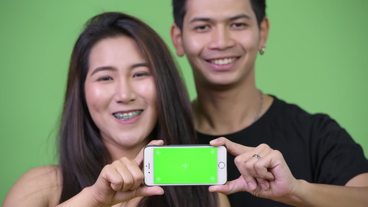 젊은 아시아 커플이 함께 전화를 보여주고 있습니다.