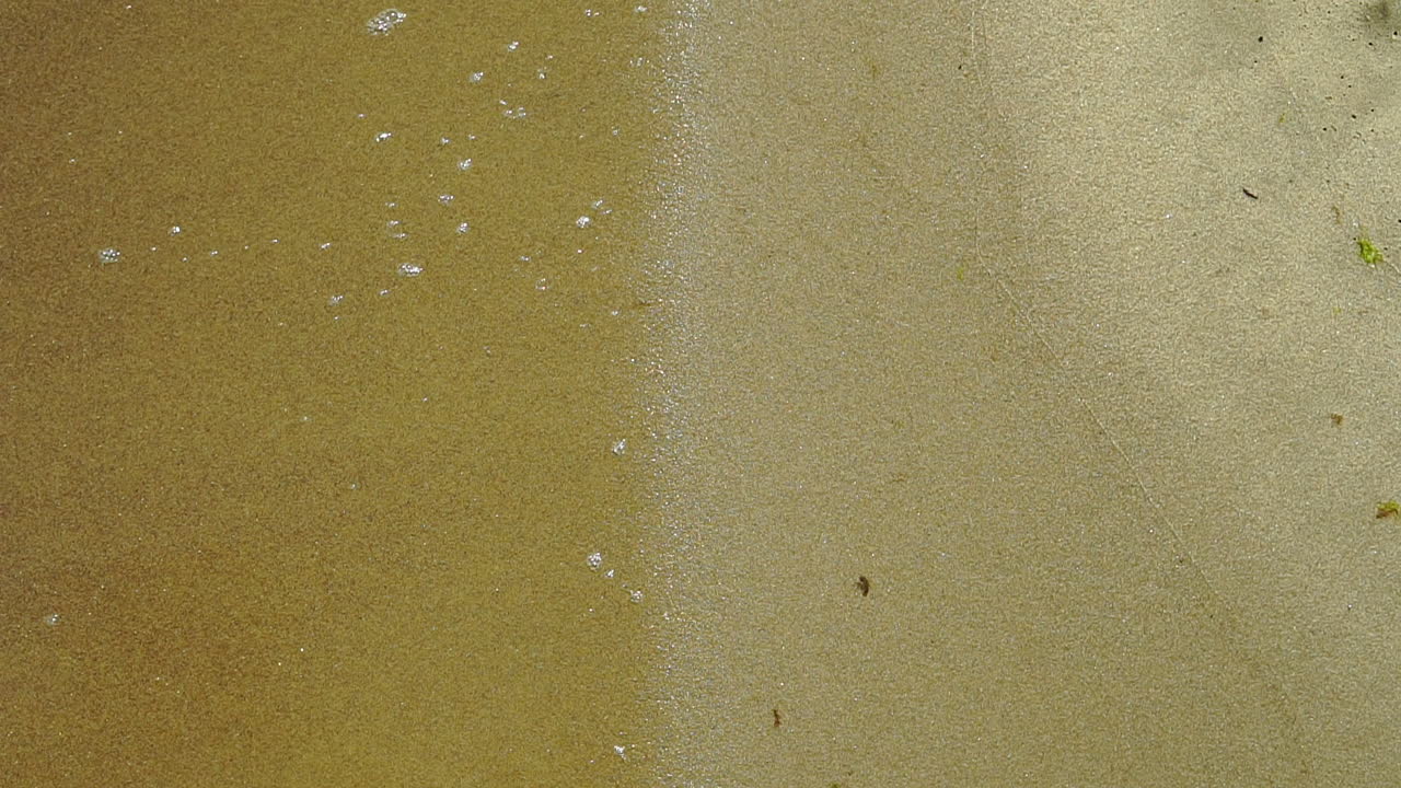 cámara lenta, vista de la orilla del mar, espuma del agua vertida en la arena, arena y agua en la costa