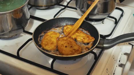 grandma, mother takes fried pork chops from the pan on a gas stove at grandma's