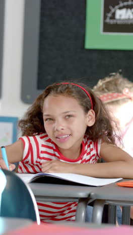 vertical video: in school, girl smiling and writing in notebook during classroom activity