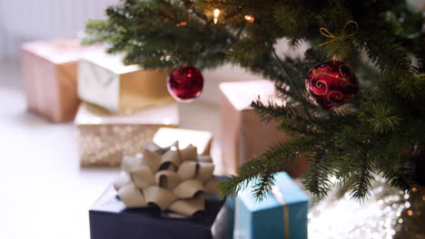 gifts arranged under a decorated christmas tree with red baubles, close up, rack focus