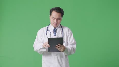 asian male doctor with stethoscope using a tablet while walking on green screen background in the hospital