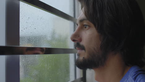 man looking out of window at rain