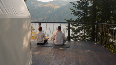 couple practices yoga near glamping tent in evening. relaxed young people finish day with meditation practice sitting in lotus pose. finding harmony