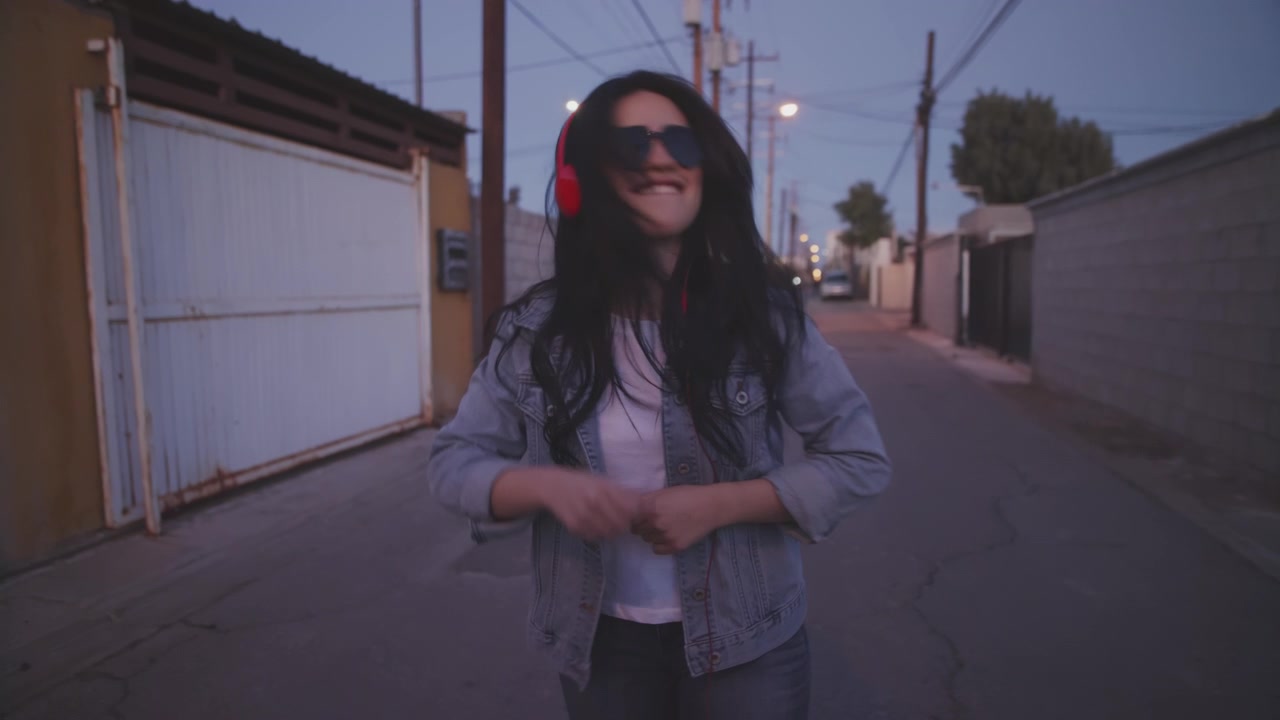 Primo piano di giovani donne felici che sorridono e ascoltano musica in un vicolo, con cuffie rosse.