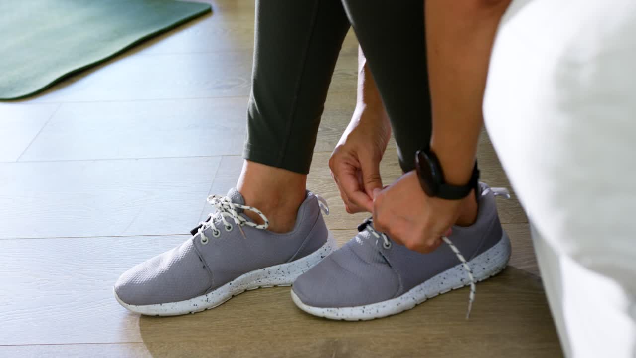 Donna afroamericana in leggings neri che allaccia i lacci fantasia delle sneakers grigie a casa per l'allenamento