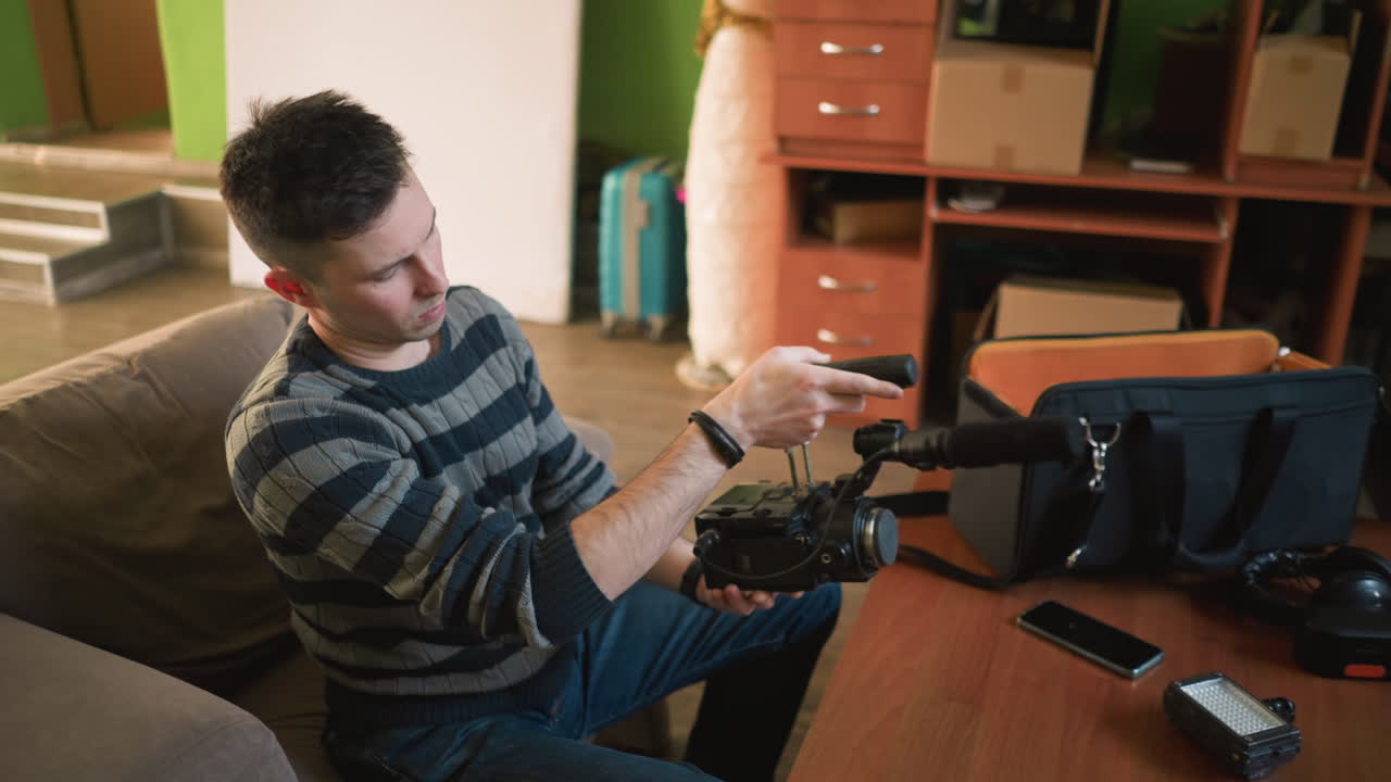 Man setting up camera and microphone in home studio, arranging filming gear on desk, preparing for content creation in modern home environment, video production