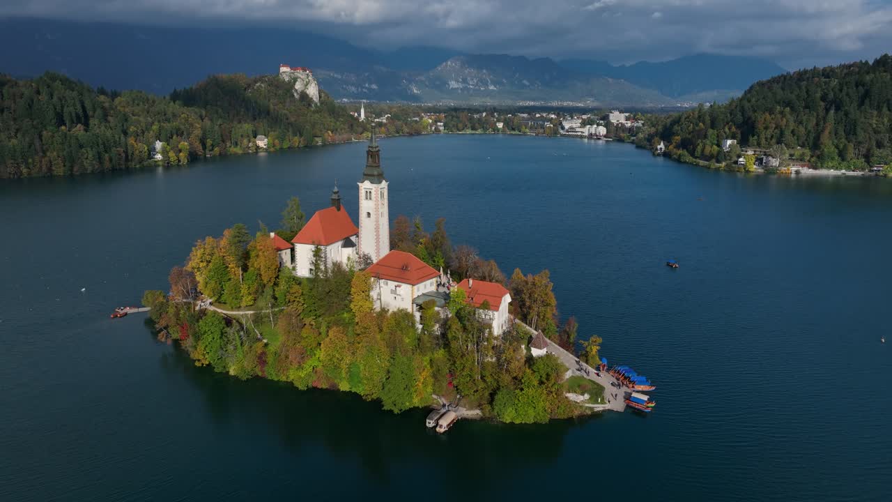 Rondvlucht met drone van het eiland Bled met kerk, omringd door een blauw meer en herfstbomen, met een zonovergoten gloed