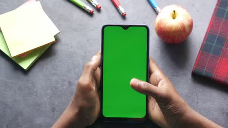 student using smartphone with green screen and school supplies on a desk