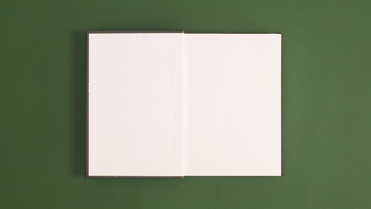 Green vintage hardcover book appear and open with copy space on green background. Stop motion flat lay