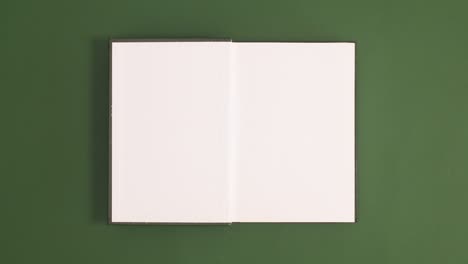 green vintage hardcover book appear and open with copy space on green background. stop motion flat lay