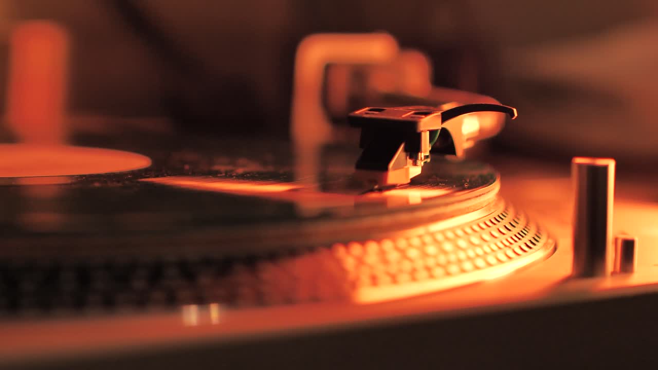 A Rotating Vinyl Record on a Turntable in the Light of a Warm Orange-Red Lamp. A dusty green colour LP Vinyl Disc Record Close-up Playing Music. Type E.
