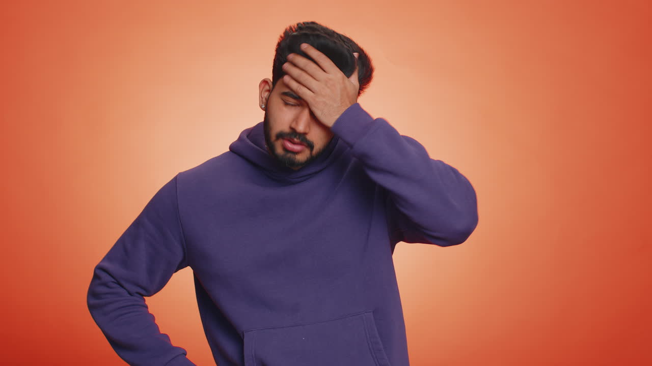 A young man wearing a purple hoodie is looking at the camera with a confused expression