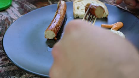 closeup of a man eating barbecue white sausage with colorful sauce or dressing and bread.