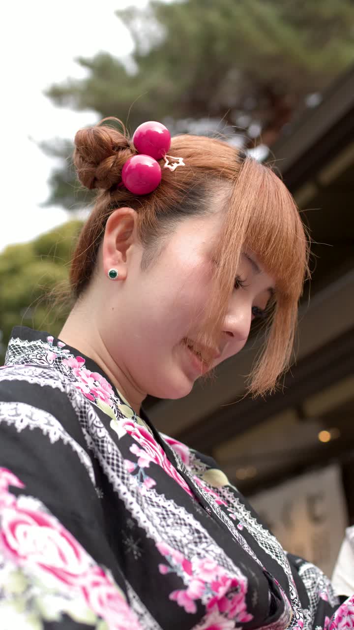 Una donna giapponese che indossa un kimono floreale scrive su una tavoletta votiva ema in legno in un santuario.