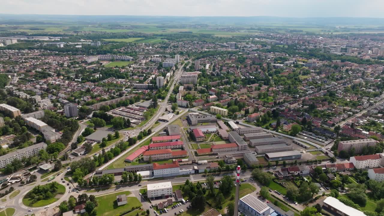 Aerial pull-back from entrance gate to reveal full prison complex and perimeter systems; smooth backward motion, continuous shot, daytime