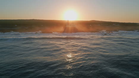 Bright sun setting down behind coastline aerial view. Ocean waves washing coast