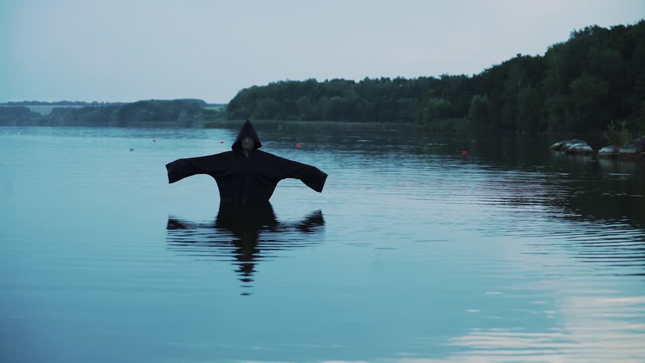Horror woman soaking in water river. Scary figure in black mantle.