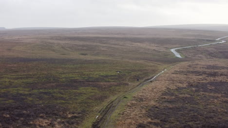 Runner-Athlete-Jogging-Over-Moorland-Path-Terrain-with-Road-in-Background---Aerial-Drone-Rising-Shot-UK-4K