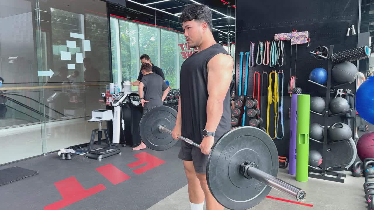 A person performs barbell deadlifts in a modern gym, showcasing strength and focus in a well-lit environment