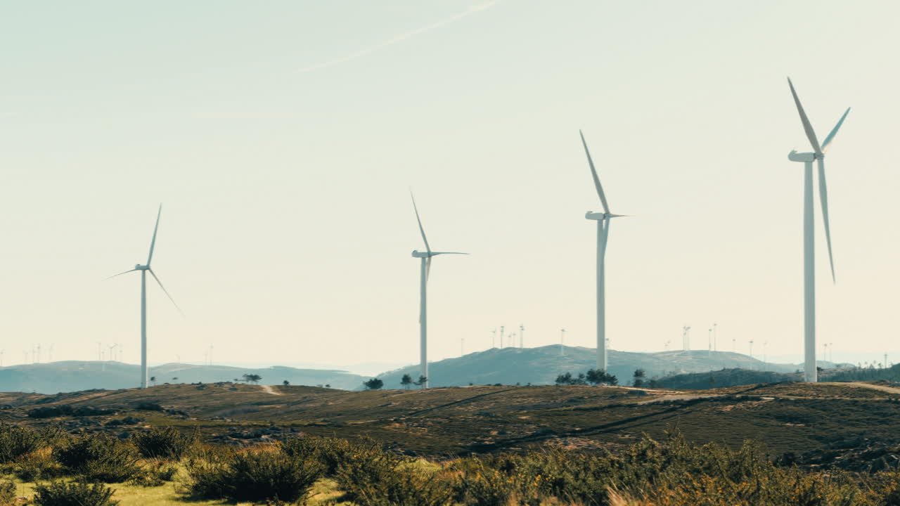 una vista panorámica de las turbinas eólicas paradas contra un telón de majestuosas montañas en un día soleado