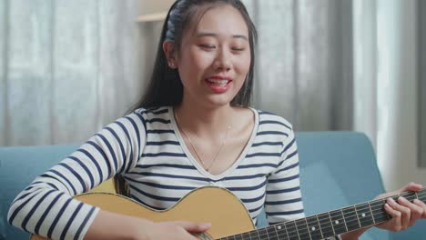 mujer joven cantando y tocando la guitarra acústica en casa