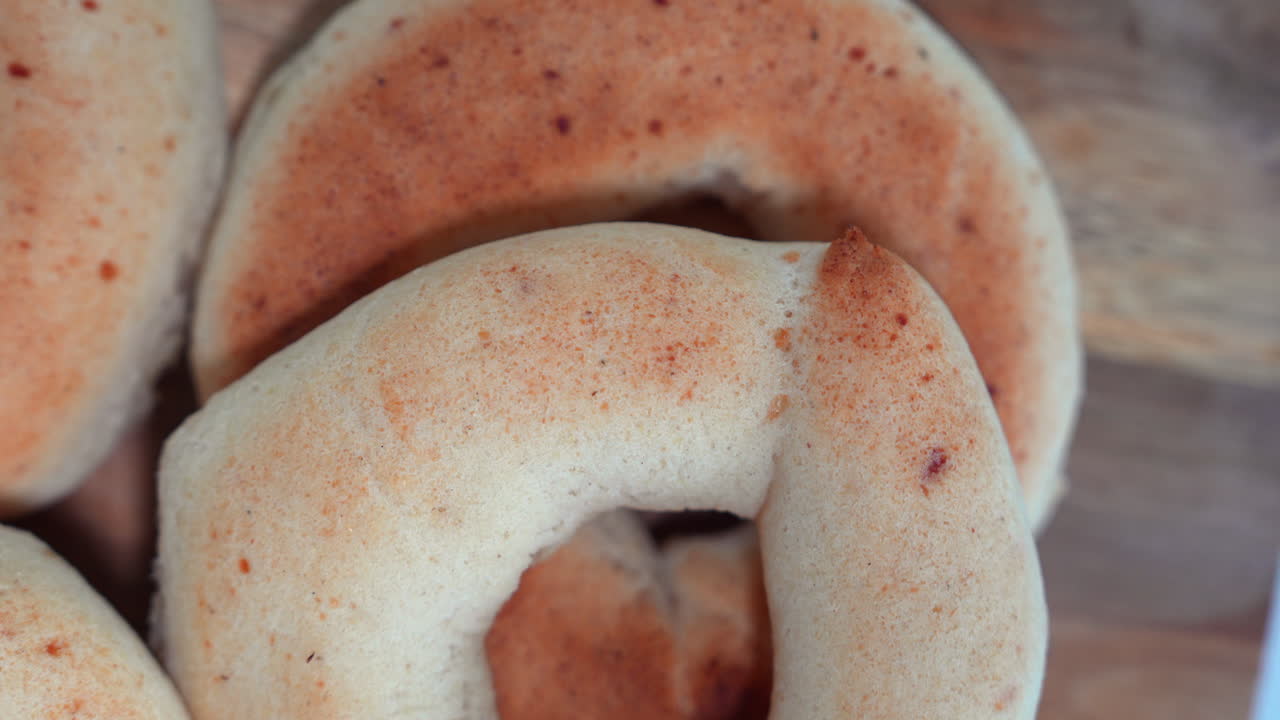 Detailed close-up of freshly baked pandebono on a rustic wooden surface. Soft lighting enhances the texture and golden crust of the bread, capturing the essence of Colombian cuisine