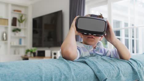 happy caucasian boy at home, sitting on couch wearing vr headsets and smiling